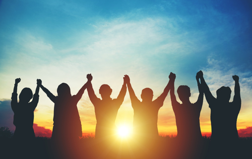 Silhoutte of a group of people holding hands up in the air at sunset